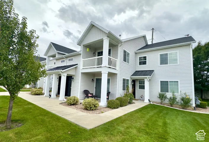 Two-story exterior featuring light-colored horizontal siding, dual-level covered porches with white columns, a dark metal roof accent, and a concrete walkway