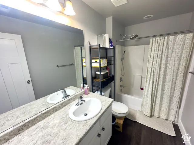 Full-width vanity with dual undermount sinks, stone-finish countertop, expansive wall-mounted mirror, wood-finish flooring, and a combined tub and shower unit