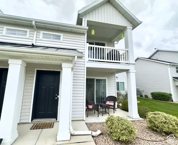 Exterior featuring light-colored horizontal siding, a covered ground-level concrete patio, a second-story balcony with a white railing, and square columns