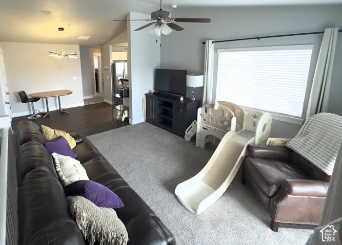 Vaulted ceilings, large picture window with blinds, ceiling fan with integrated lighting, modern multi-arm pendant light, and contrasting wood-finish flooring