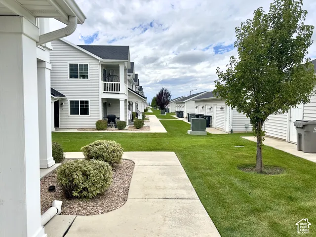 Multi-unit exterior featuring white horizontal siding, concrete walkways, green lawns, and established landscaping