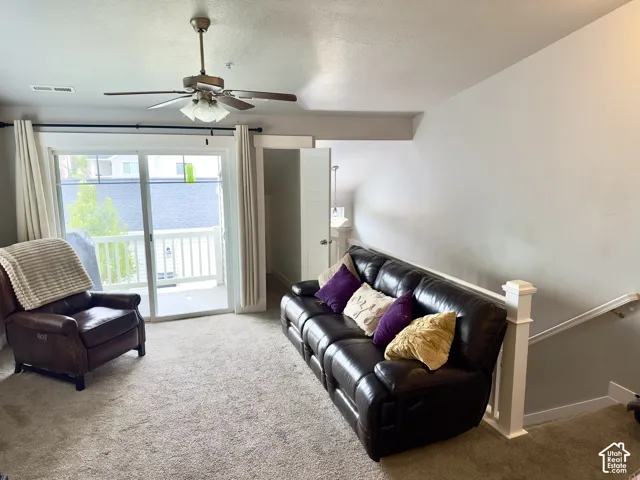 Sloped ceiling featuring a centrally mounted ceiling fan with integrated lighting, sliding glass door with balcony access, and a painted wooden handrail with balusters
