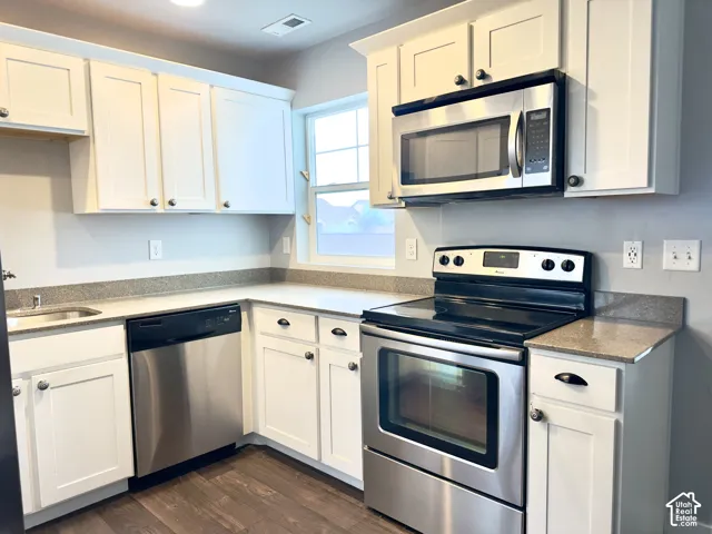 Kitchen featuring white shaker-style cabinetry, stone-finish countertops, stainless steel appliances, and wood-finish flooring