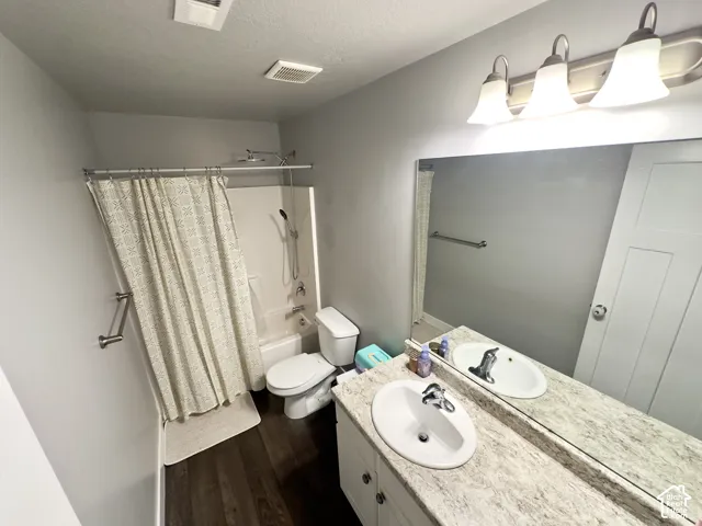 Bathroom featuring wood-finish flooring, a vanity with a neutral-tone countertop and integrated sink, a full-width wall mirror, and a tub-shower combination with a hand-held showerhead fixture