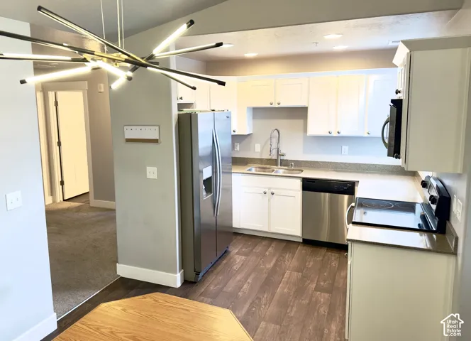 Kitchen featuring white cabinetry, stainless steel appliances, wood-finish flooring, stone-surfaced countertops, and a modern multi-directional pendant light fixture