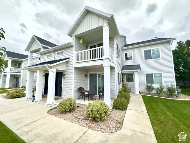 Two-story exterior featuring light-colored horizontal siding, a private balcony with white railings, columned covered entryways, and concrete walkways