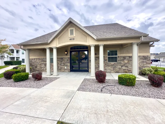 Exterior facade featuring stone veneer, stucco siding, a covered entryway with structural columns, and a double-door glass entry