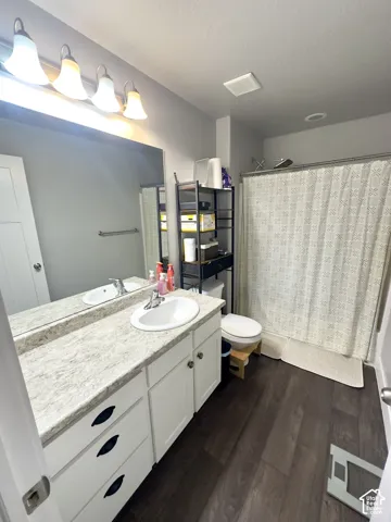 Bathroom featuring white cabinetry, stone-finish vanity countertop with integrated sink, four-light vanity fixture, and wood-finish flooring