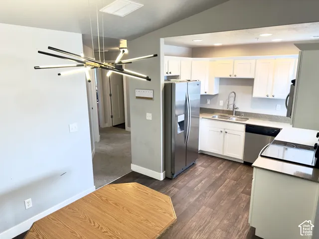 Kitchen featuring white shaker-style cabinetry, stainless steel appliances, a dual-basin undermount sink with a gooseneck faucet, and wood-finish flooring, accented by a contemporary multi-arm sputnik chandelier