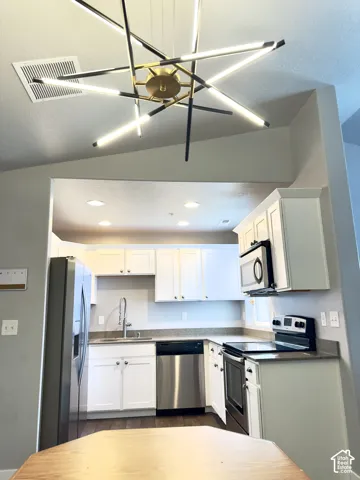 Geometric starburst pendant chandelier, white shaker-style cabinetry, stainless steel appliances, recessed ceiling lighting, and solid-surface countertops