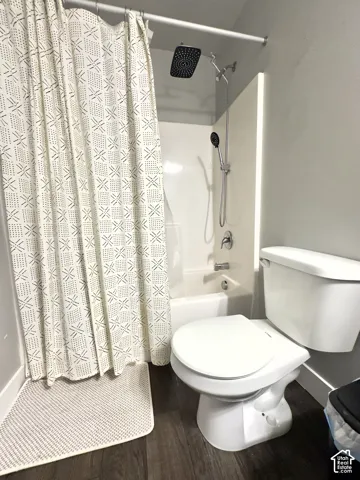 Bathroom featuring wood-finish flooring, a white bathtub with a wall-mounted surround, a rainfall showerhead, a detachable handheld sprayer, and a chrome mixing valve