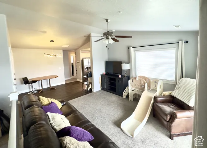 Open-concept living space featuring vaulted ceilings, wood-finish flooring, a ceiling fan with integrated lighting, and a modern multi-arm chandelier