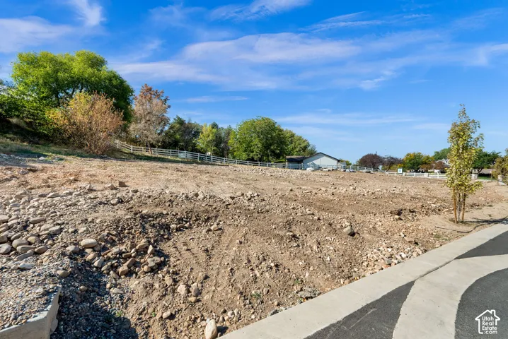 Expansive lot featuring a cleared building site, mature trees, a white perimeter fence, and a paved pathway