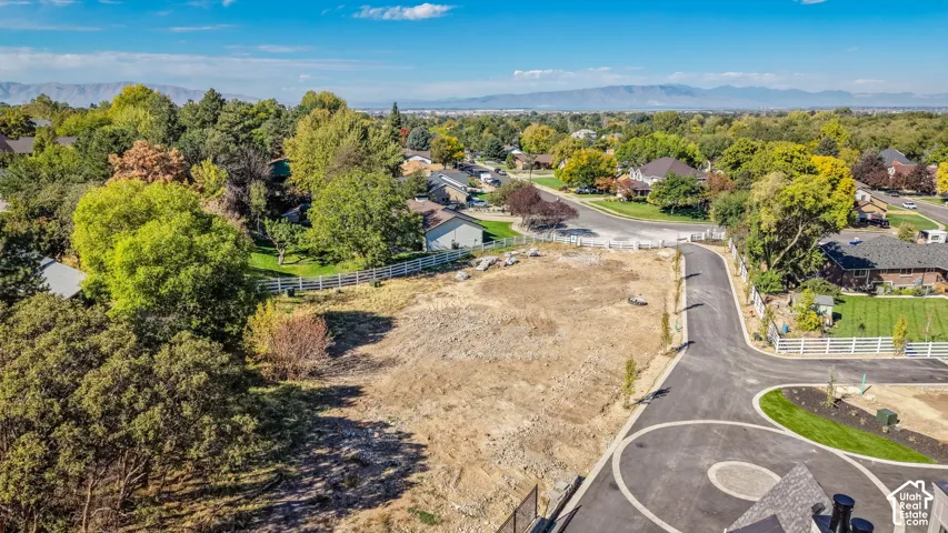 Expansive lot featuring a newly paved driveway with circular details, surrounding mature trees, and a distant mountain range