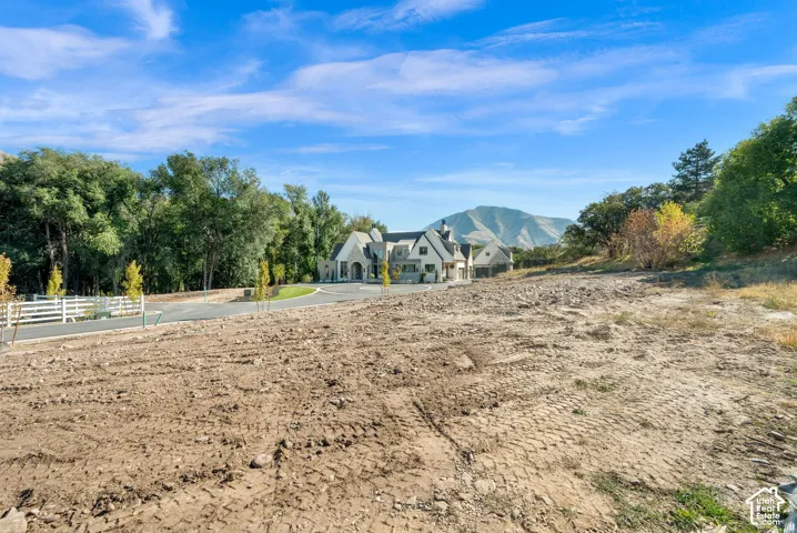 Expansive lot with a mountain backdrop, a paved driveway, and a white picket fence