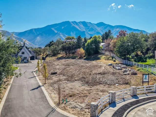 Expansive cleared lot with mountain backdrop, bordered by white fencing and a paved entryway with stone pillars