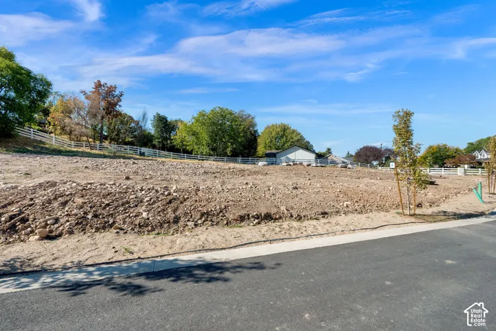 Expansive cleared lot featuring partial white fencing and young planted trees