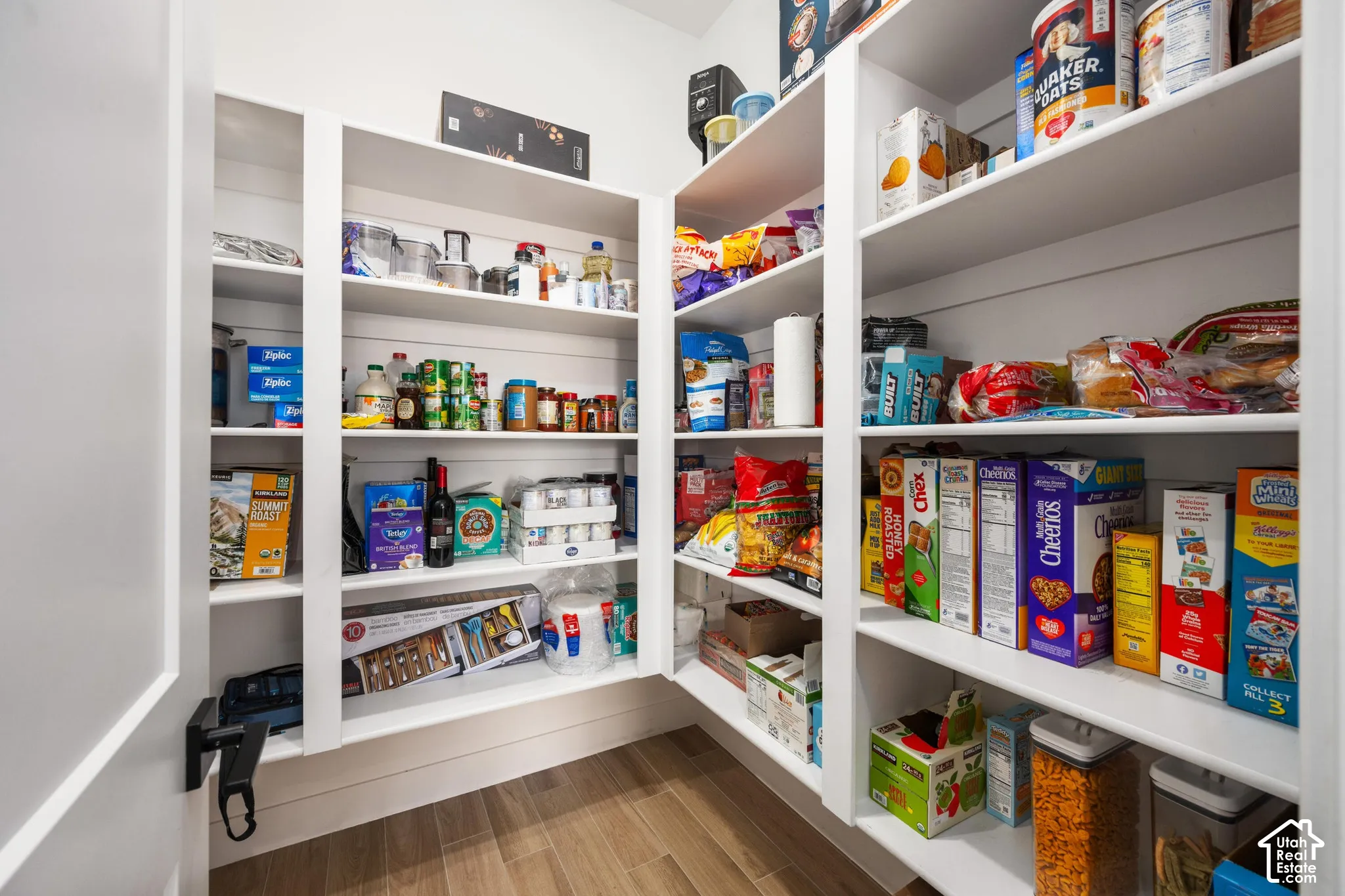 Walk-in pantry featuring white custom built-in shelving, shiplap wall detailing, and wood-finish flooring