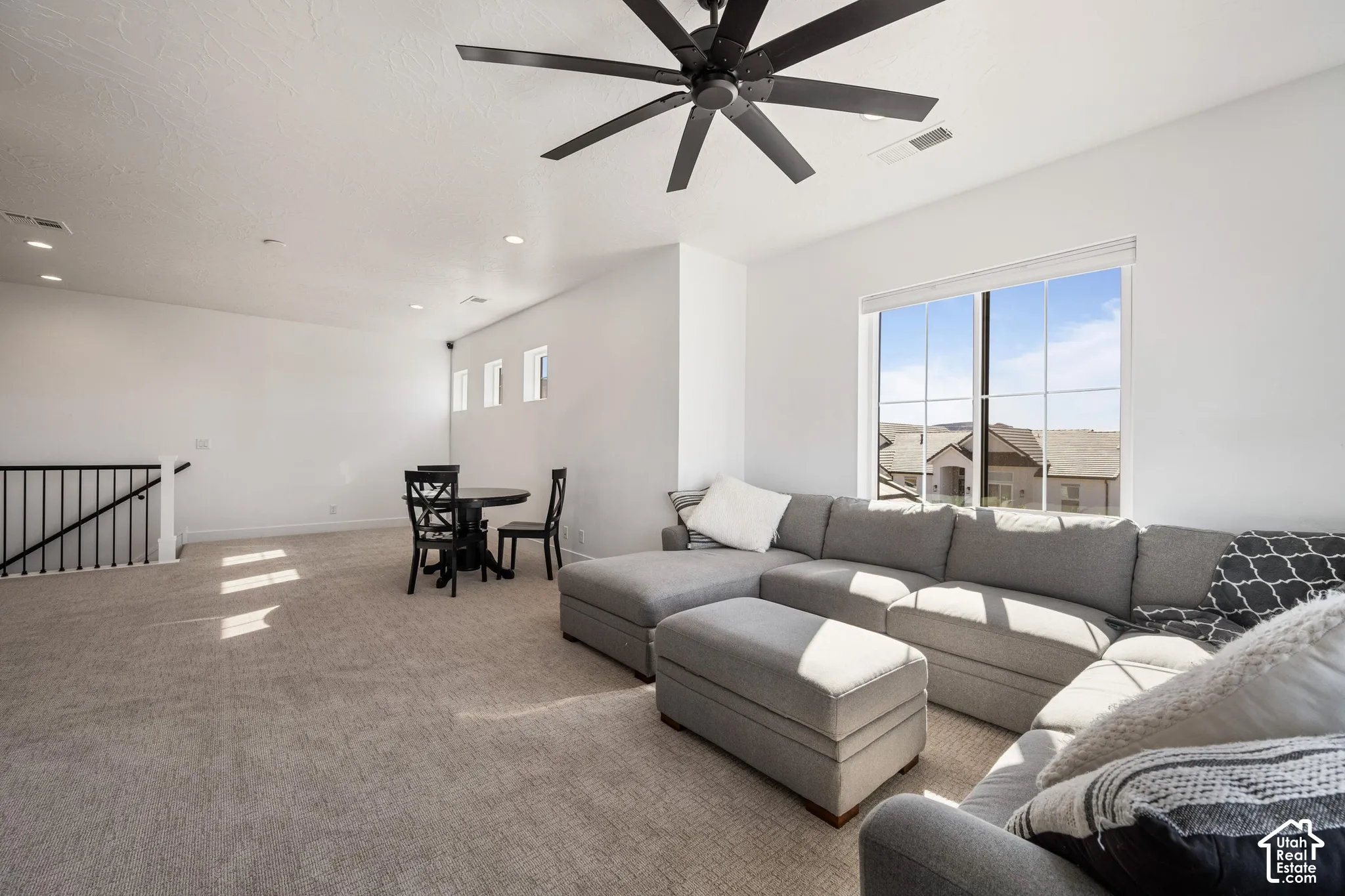Expansive space featuring neutral wall-to-wall carpeting, a large multi-pane window, recessed lighting, and a modern matte black ceiling fan