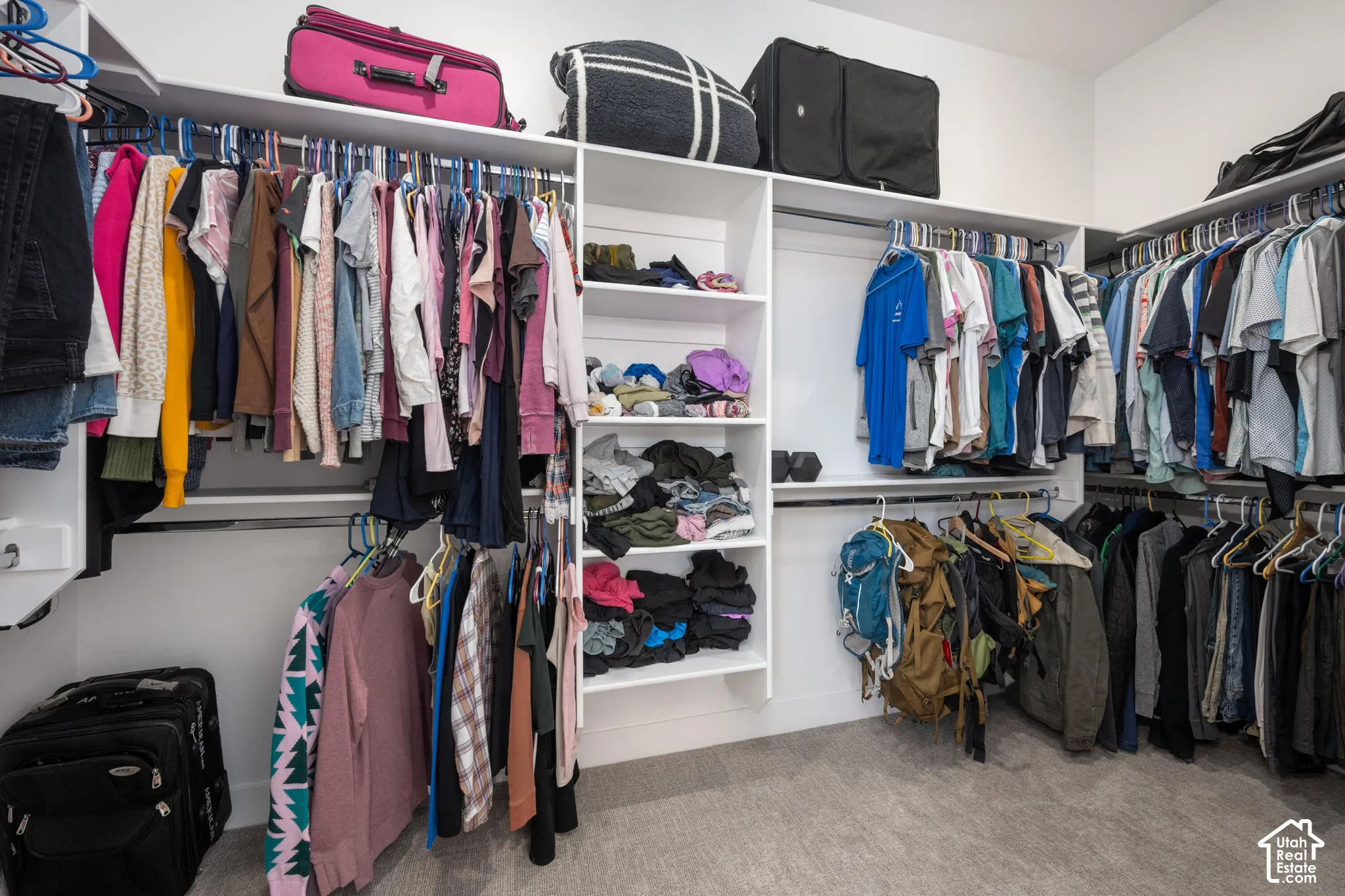 Primary Walk-in closet featuring white built-in shelving, integrated vertical storage cubbies, and multiple metal hanging rods