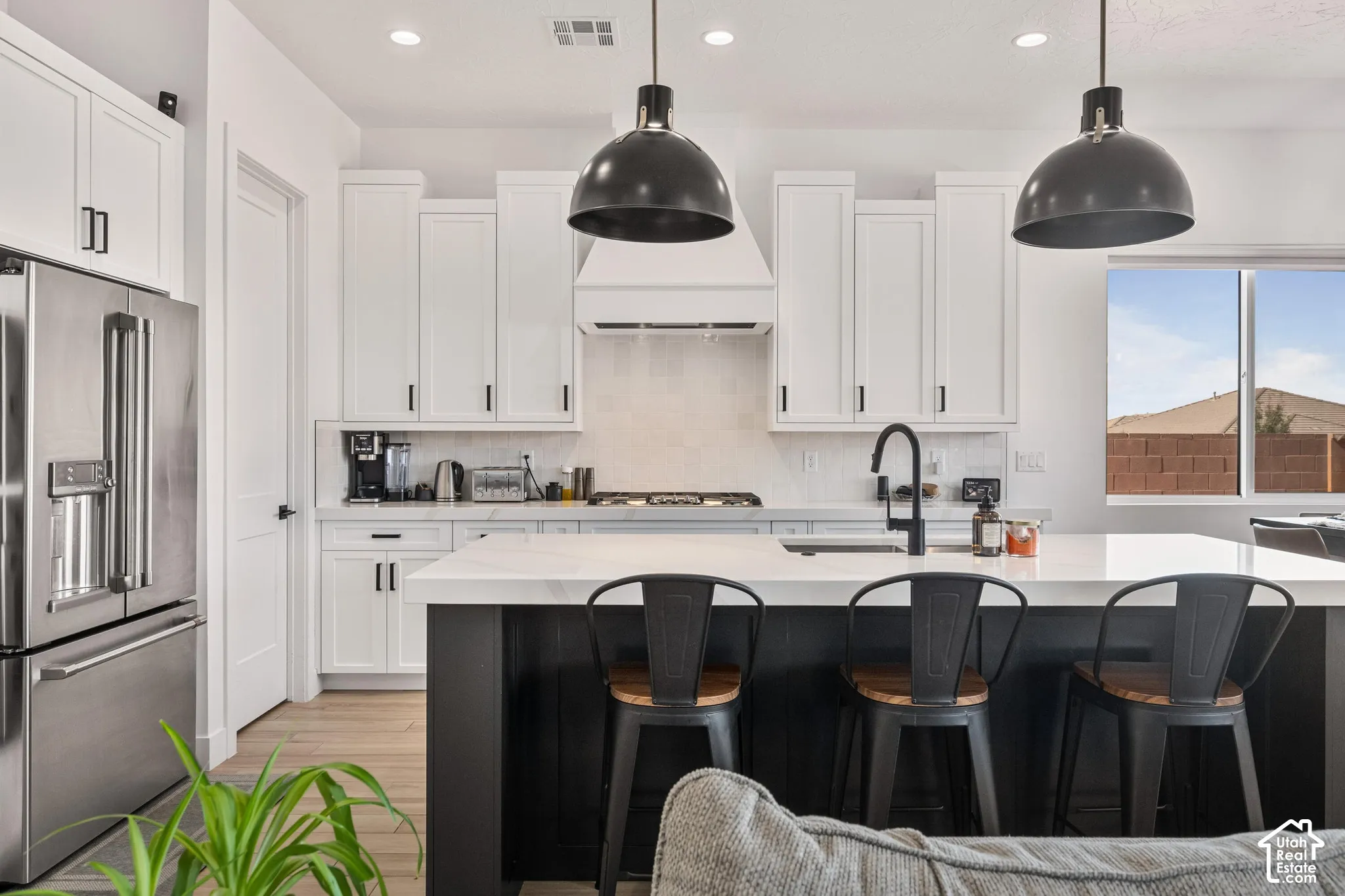 Kitchen featuring white shaker cabinetry, an expansive center island with a stone-finish countertop, dual oversized pendant lights, stainless steel appliances, and a matte black faucet