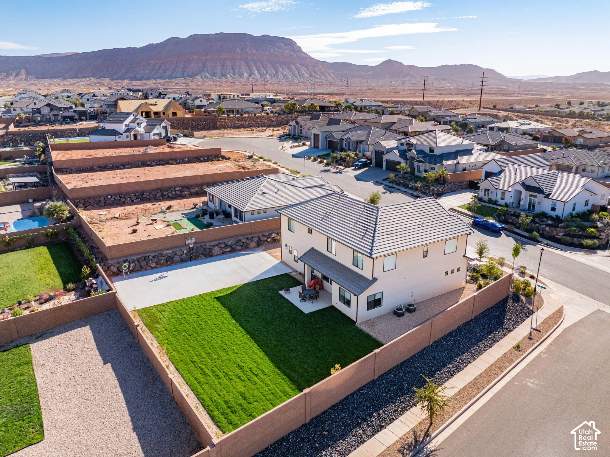 Aerial perspective featuring a two-story residence with a concrete-tile roof, expansive fenced backyard, manicured lawn, concrete patio, and prominent mountain backdrop