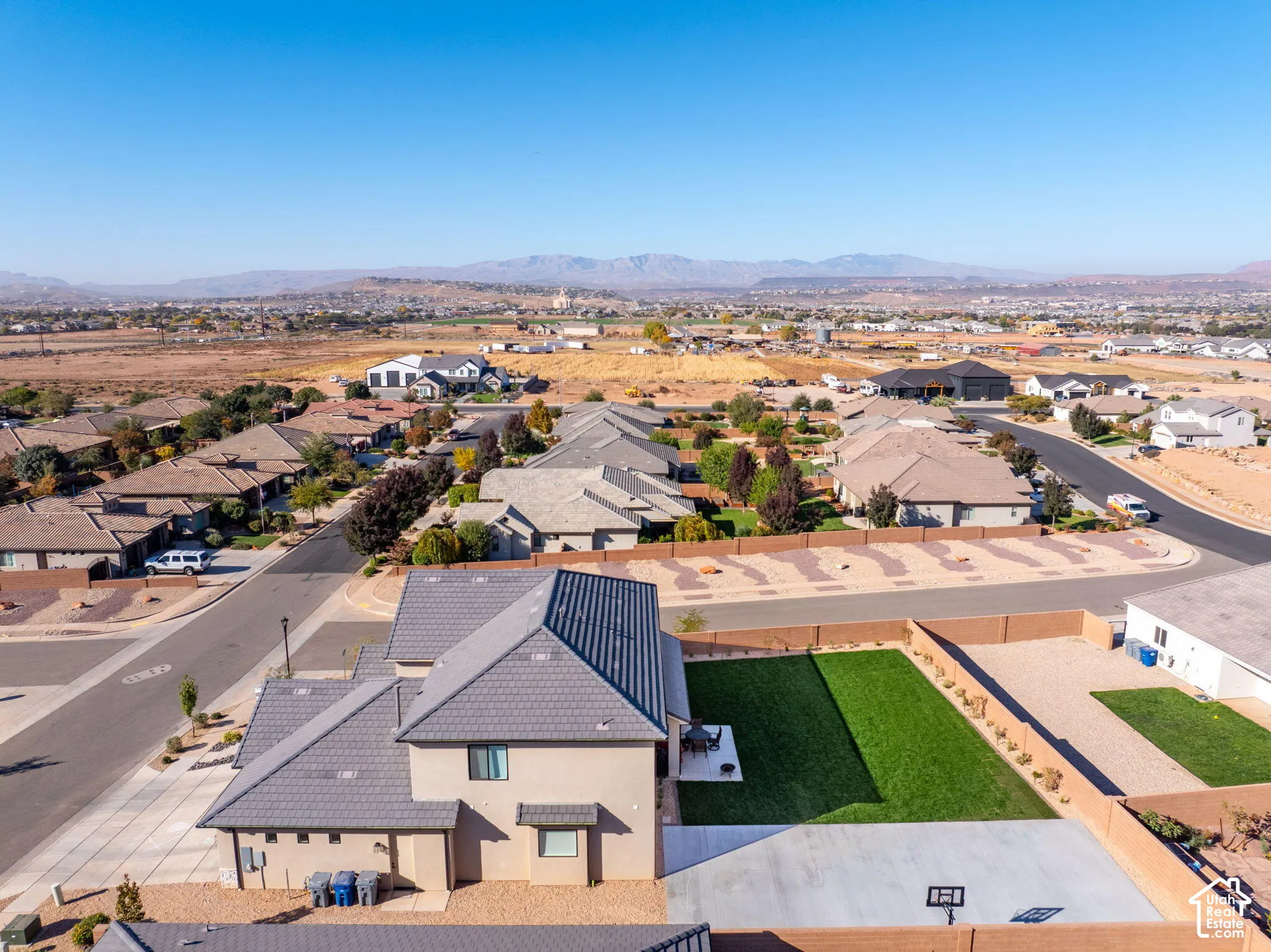 Aerial perspective of a multi-level residence featuring a concrete tile roof, a private backyard with manicured lawn, a concrete patio, and surrounding mountain scenery