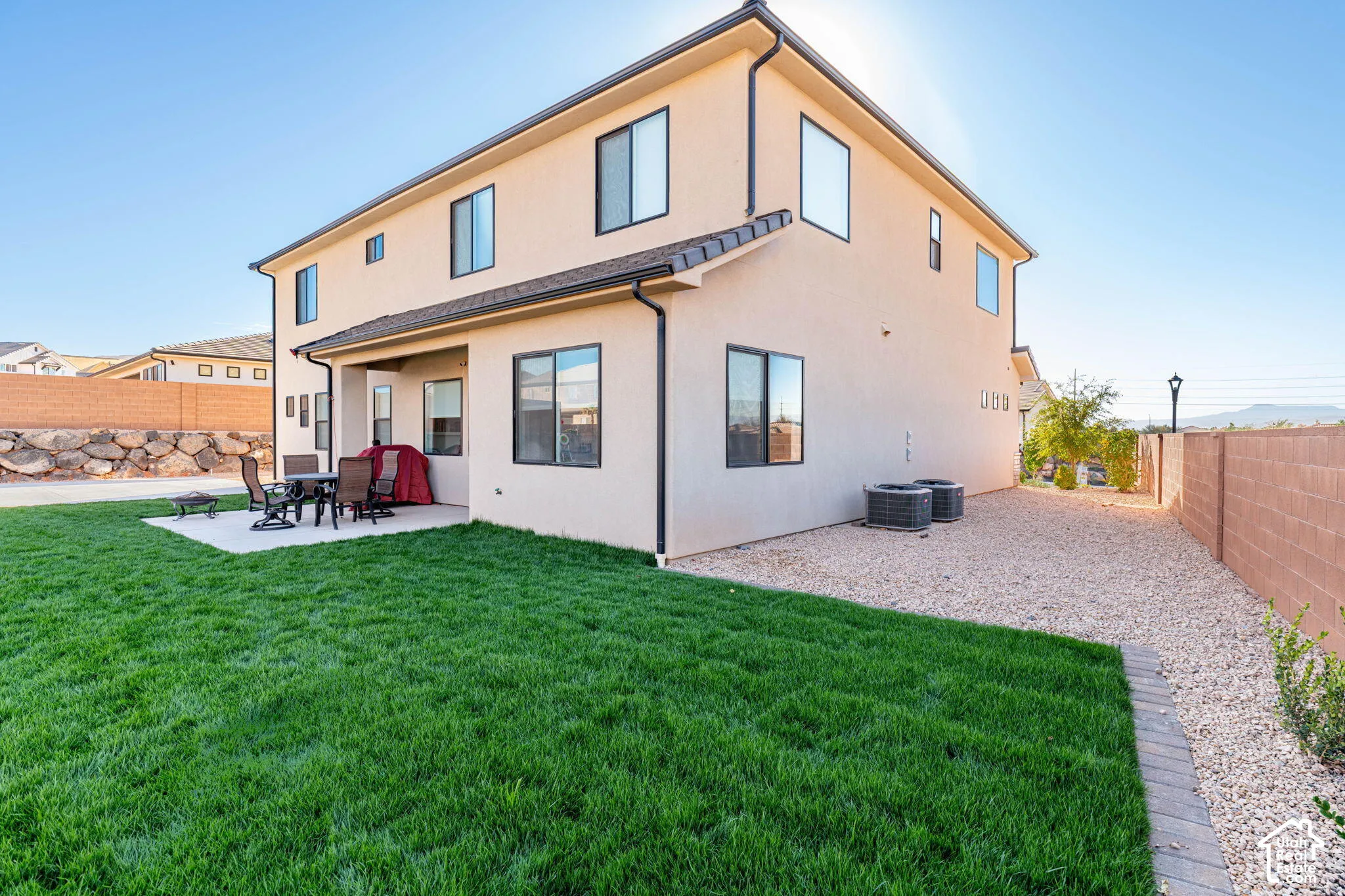 Stucco exterior featuring a covered patio, manicured lawn, stone retaining wall, and gravel side yard