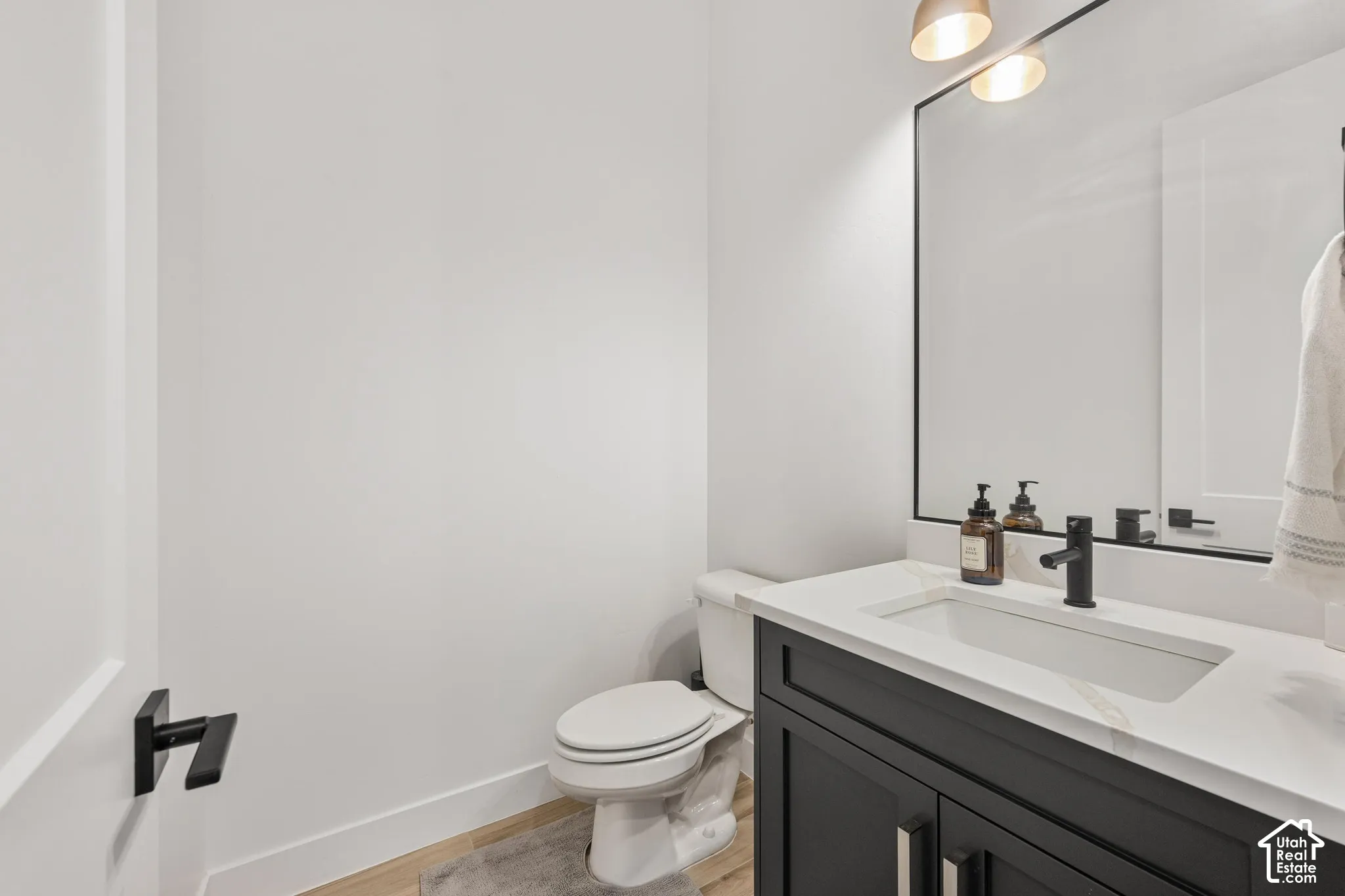 Dark-toned vanity with a rectangular sink, crisp white countertop, matte black faucet, and a large framed mirror with overhead lighting