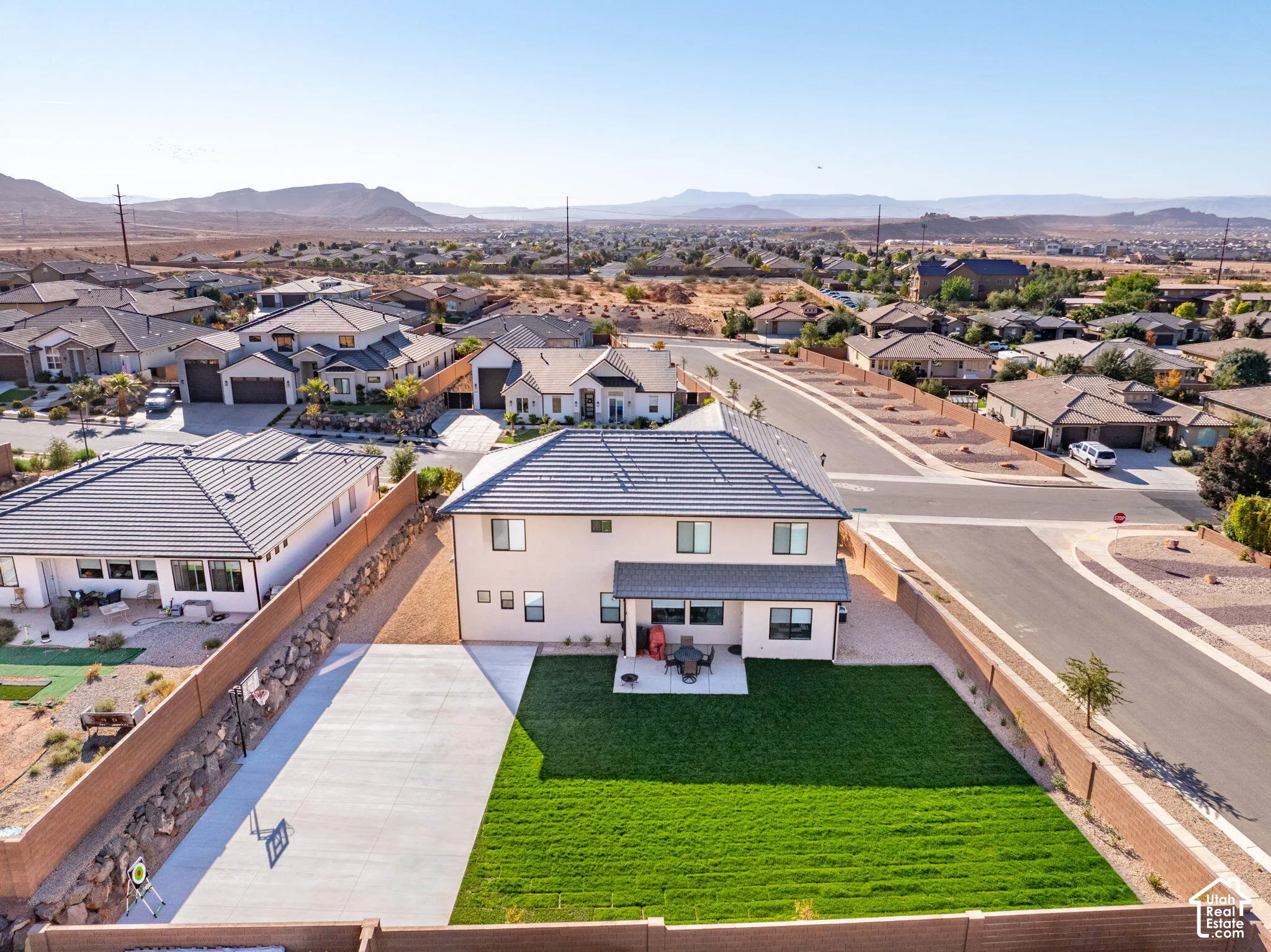 Two-story residence featuring a tile roof, an expansive rear lawn, a concrete patio, a stone retaining wall, and a multi-car paved side apron