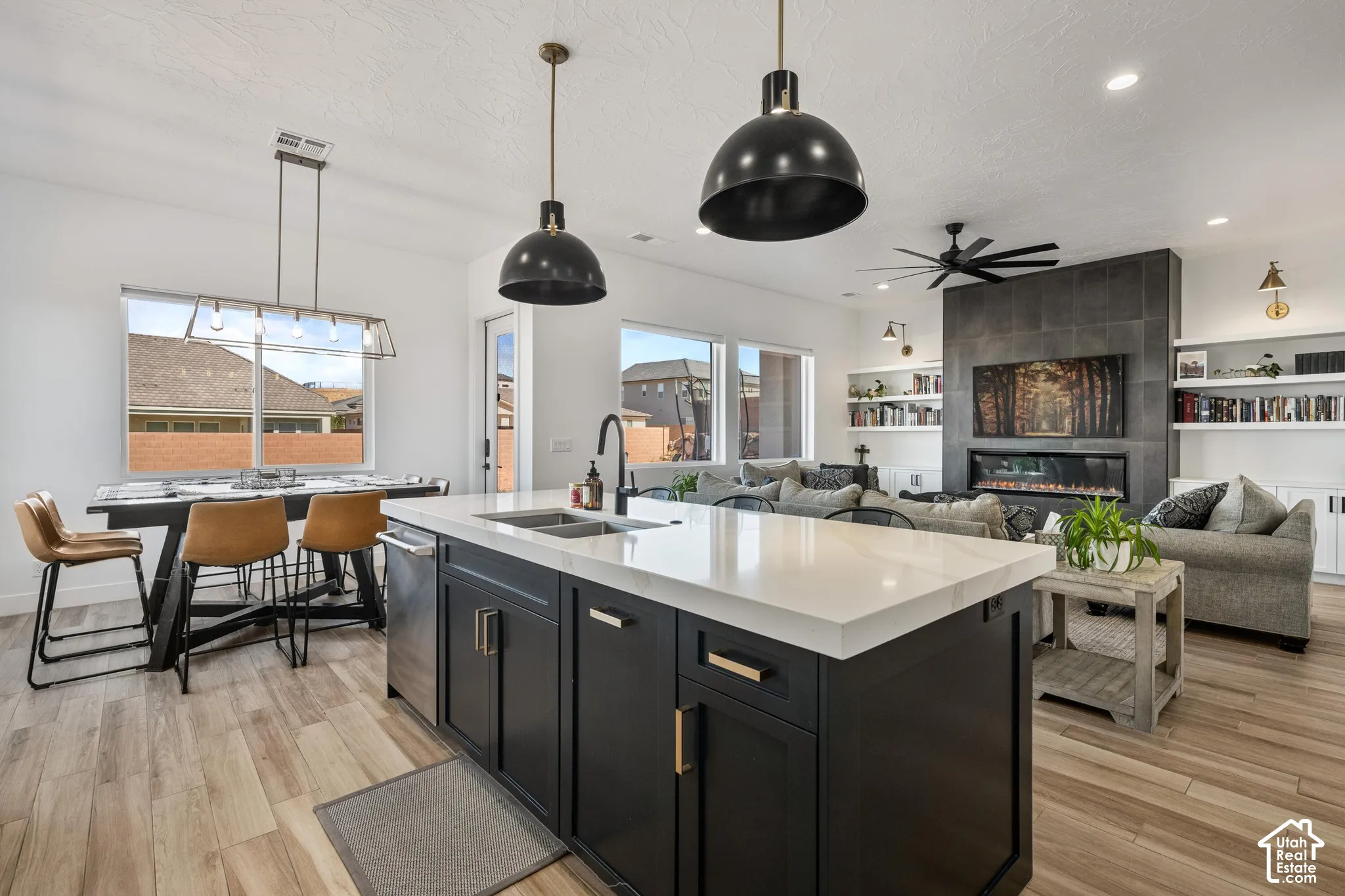 Kitchen featuring a central island with a solid surface countertop, dark cabinetry, wood-finish flooring, matte black pendant lighting, and an integrated fireplace with tile surround
