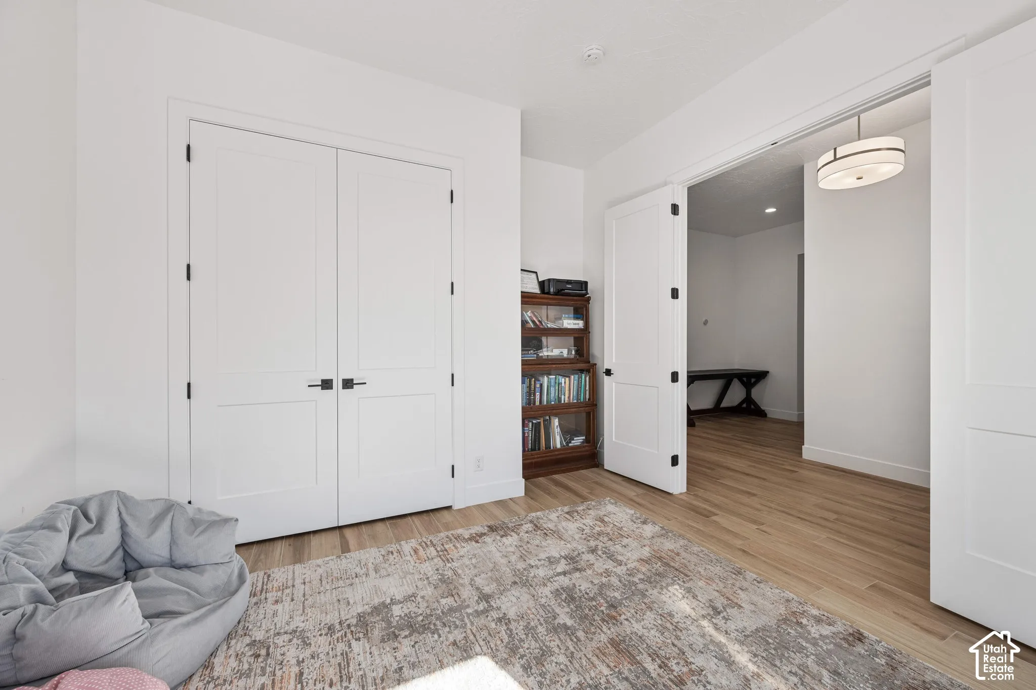Flex bed/office Wood-finish flooring, white shaker-style double doors with matte black hardware, and a contemporary drum pendant light fixture