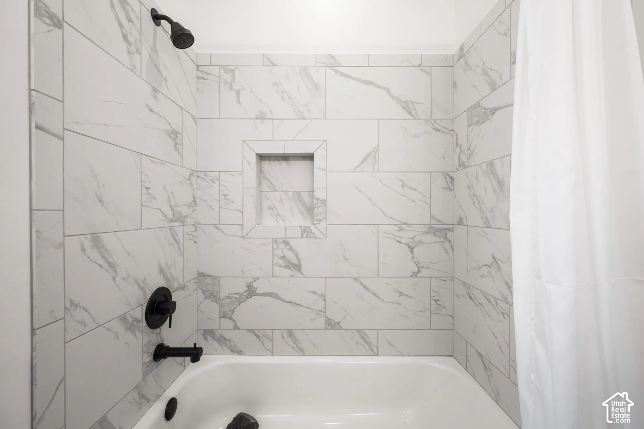 Bathtub alcove featuring large-format stone-patterned wall tile, a built-in recessed tiled niche, and matte black fixtures