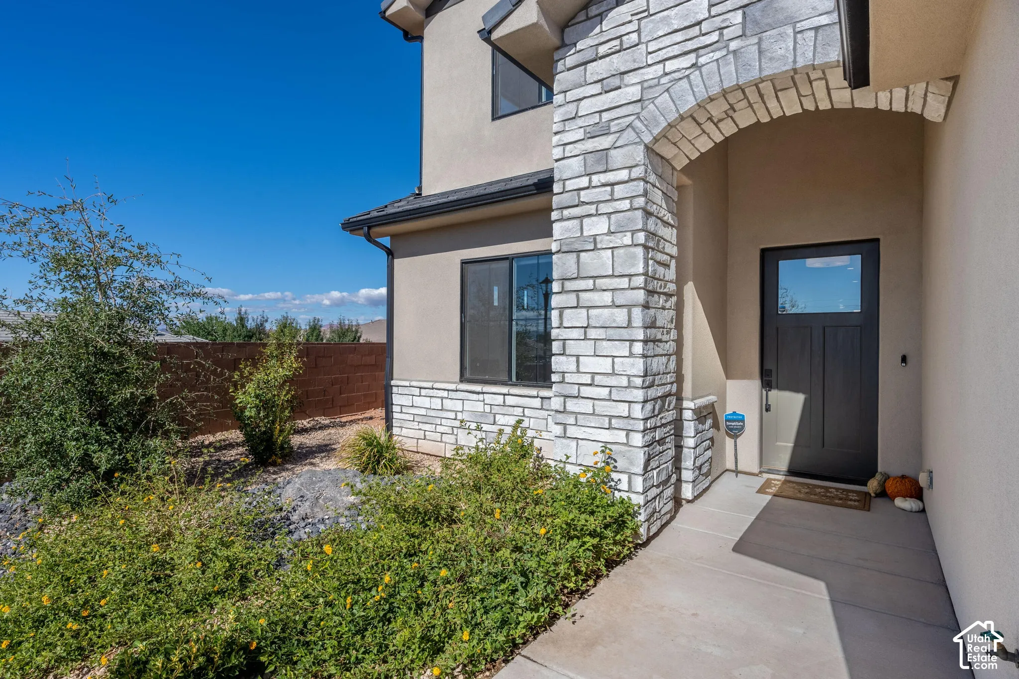 Exterior entryway featuring a stone veneer arched portico, stucco siding, and a dark-toned door with glass inset