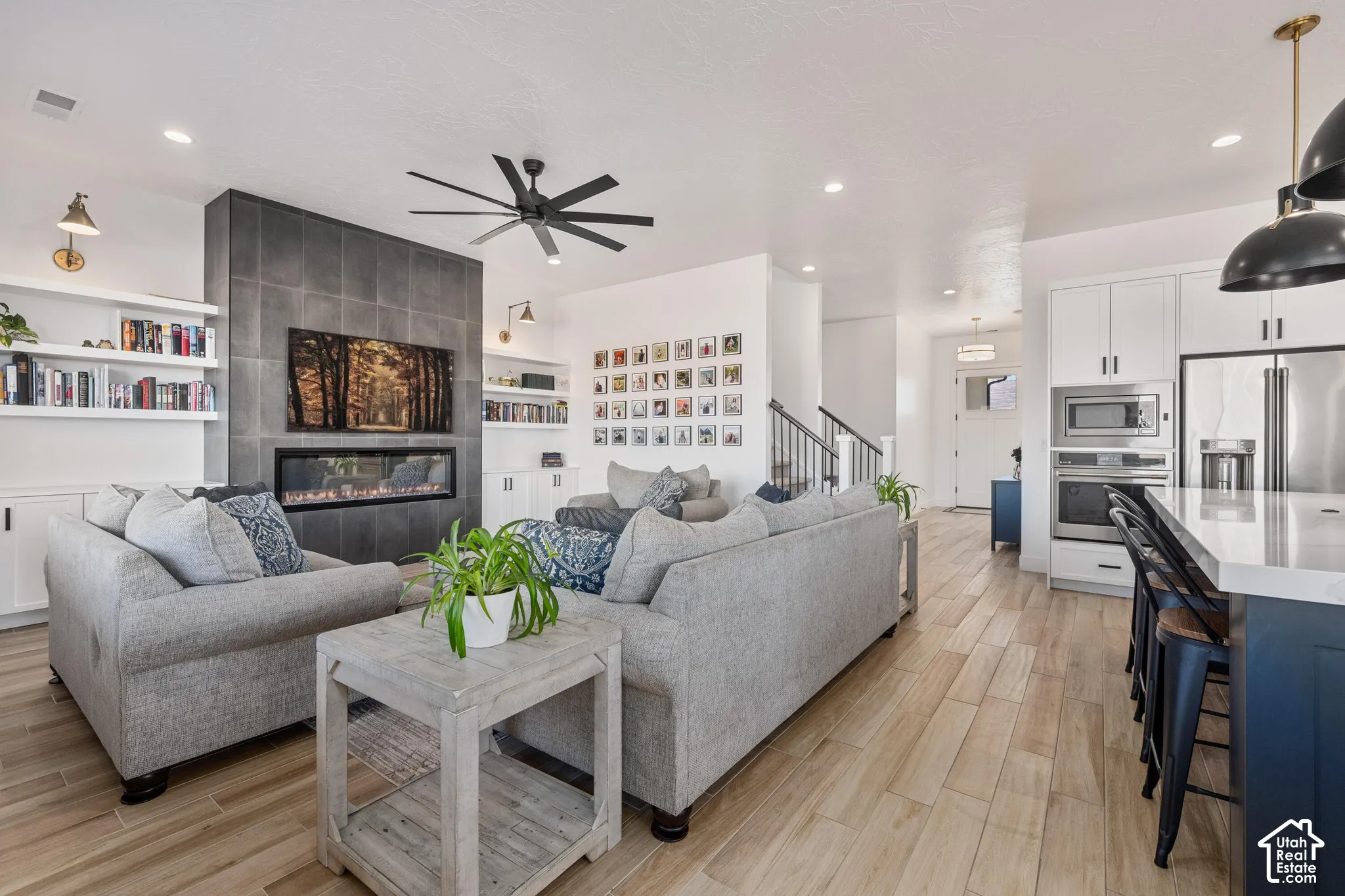 Linear gas fireplace with floor-to-ceiling tile surround, wood-finish flooring, built-in shelving, recessed lighting, and stainless steel wall-mounted oven