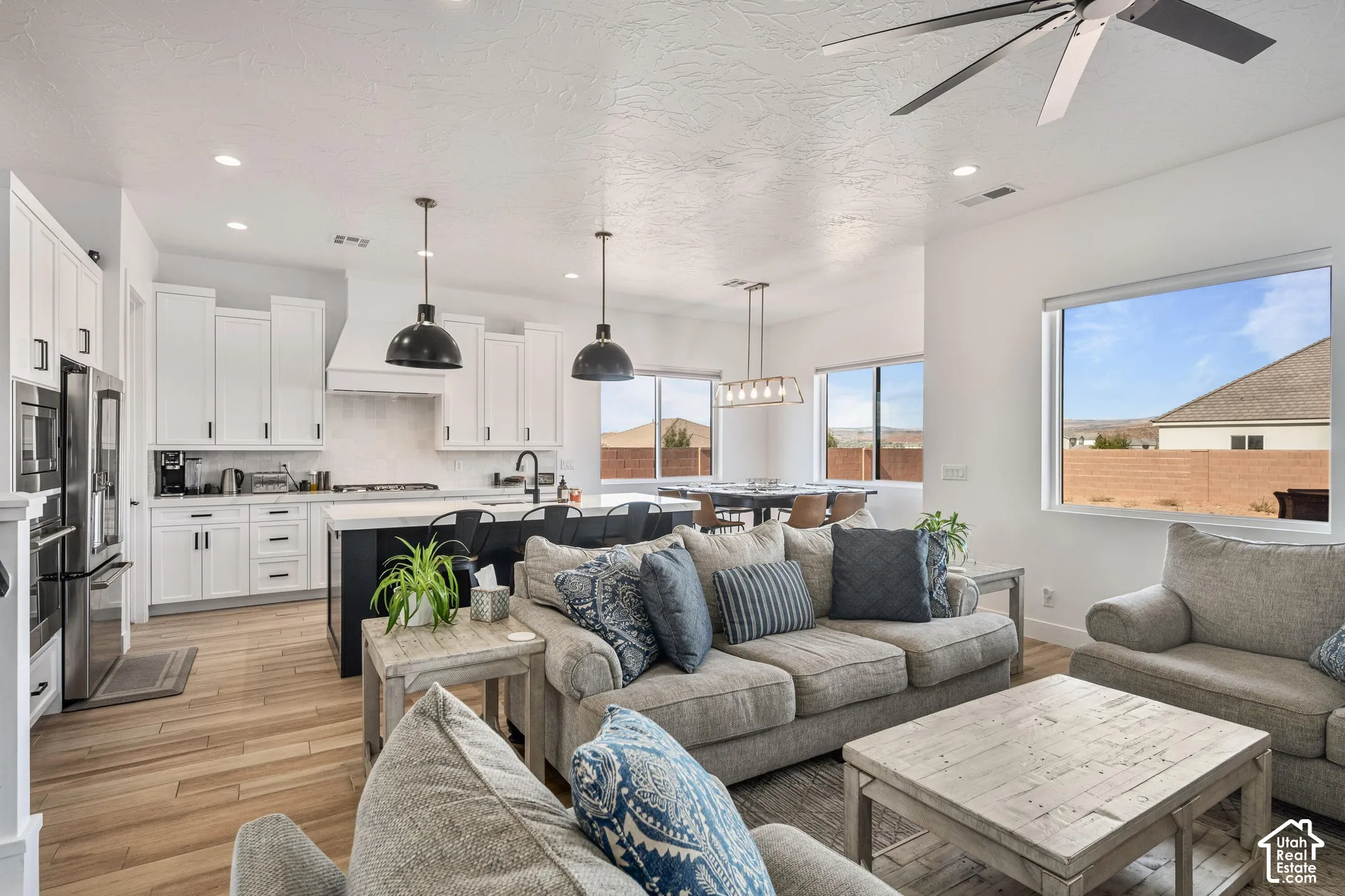 Open-concept kitchen featuring white shaker-style cabinetry, a contrasting dark kitchen island with a light-toned countertop, wood-finish flooring, matte black pendant lighting, and recessed ceiling lighting