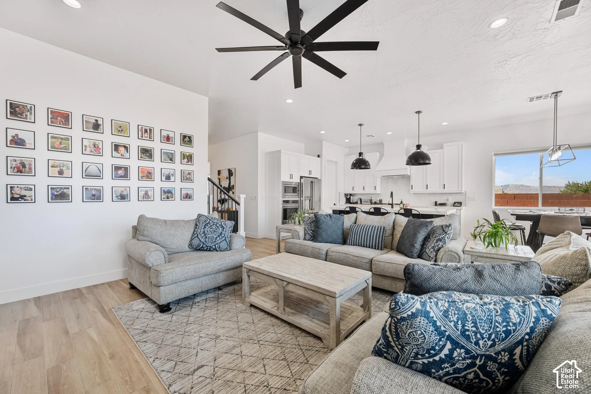 Open-concept interior featuring light wood-finish flooring, a contemporary matte black ceiling fan, recessed lighting, and a kitchen equipped with white cabinetry and integrated stainless steel appliances