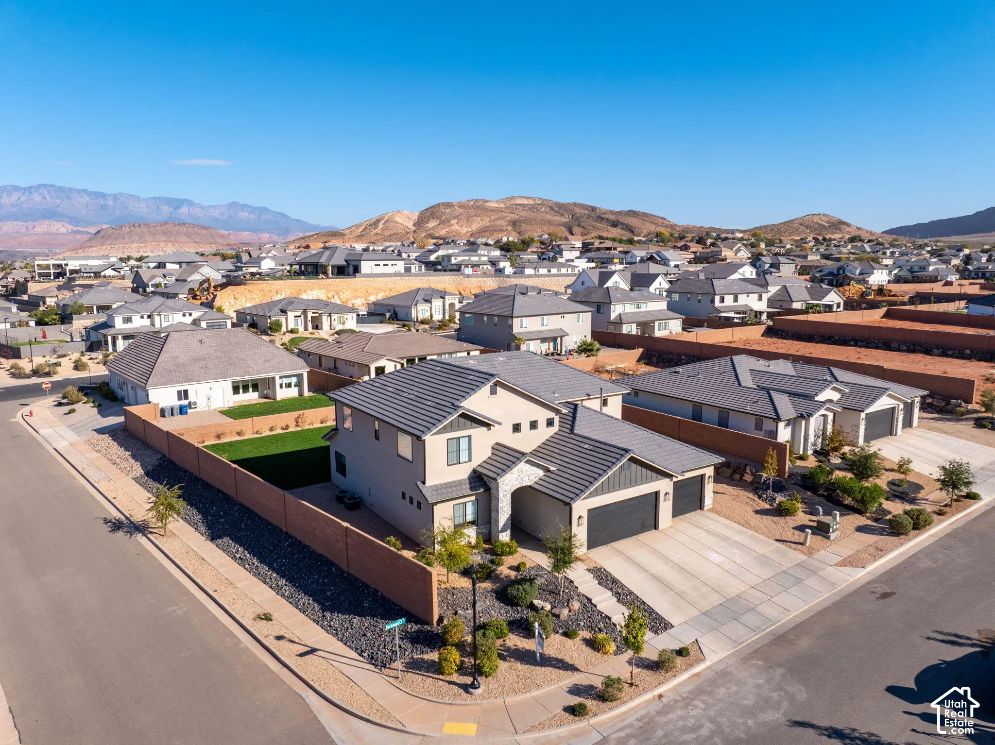 Two-story residence featuring a tile roof, stucco and stone exterior, two-car garage, and a fenced backyard with a grass lawn, set against a mountain backdrop