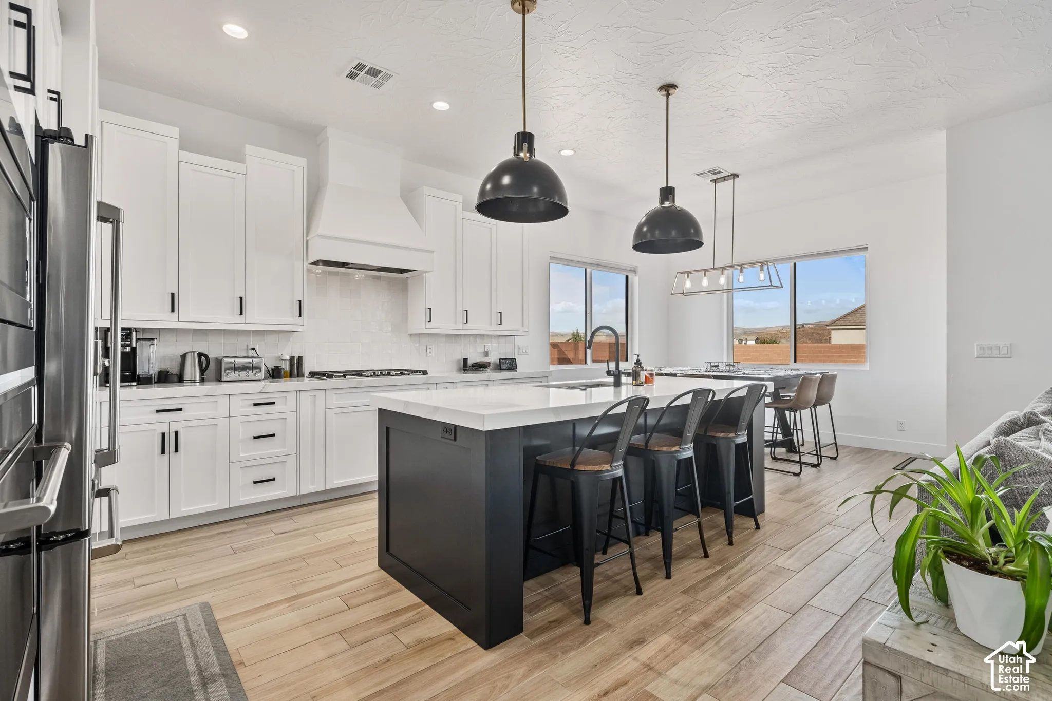 Kitchen featuring white shaker-style cabinetry, center island with stone-finish countertop, stainless steel double wall oven, wood-finish flooring, and industrial-style pendant lighting