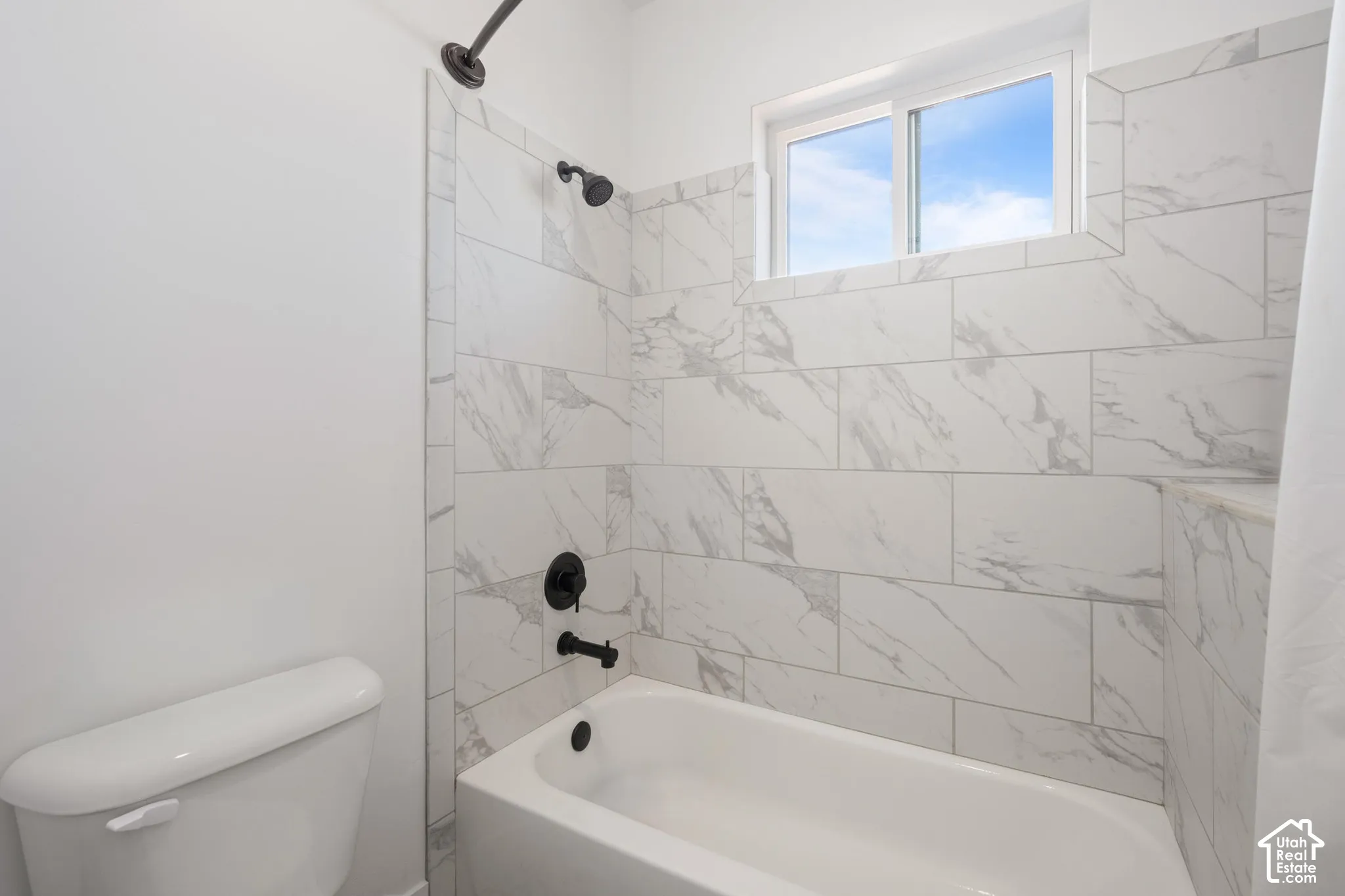 Bathroom featuring a white porcelain tub, matte black shower and tub fixtures, and floor-to-ceiling large-format stone-patterned wall tile
