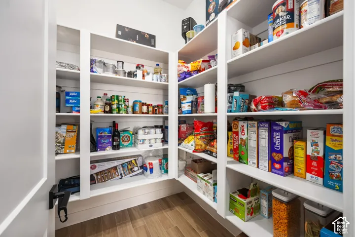 Walk-in pantry featuring white custom built-in shelving, shiplap wall detailing, and wood-finish flooring