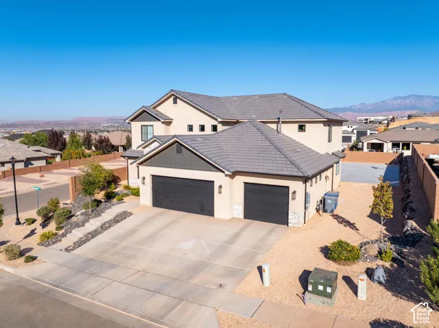 Multi-level exterior featuring stucco siding, a concrete tile roof, a three-car garage, and desert-style landscaping set against a mountain backdrop