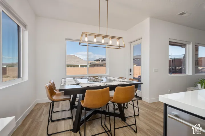 Kitchen area featuring light wood-finish flooring, rectangular geometric pendant lighting, multiple oversized windows, and high-contrast cabinetry with solid-surface countertops