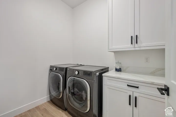 Adjacent to Primary bedroom Laundry space featuring white shaker-style cabinetry, stone-surface countertop, wood-finish flooring, and matte black hardware