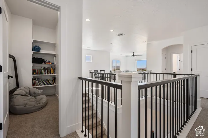 Interior area featuring recessed lighting, carpeted flooring, a metal stair railing with a wooden handrail, and a built-in shelving unit