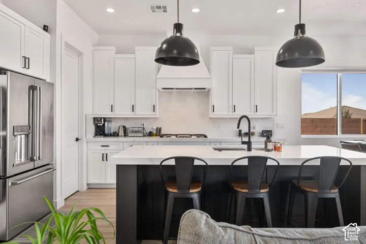 Kitchen featuring white shaker cabinetry, an expansive center island with a stone-finish countertop, dual oversized pendant lights, stainless steel appliances, and a matte black faucet