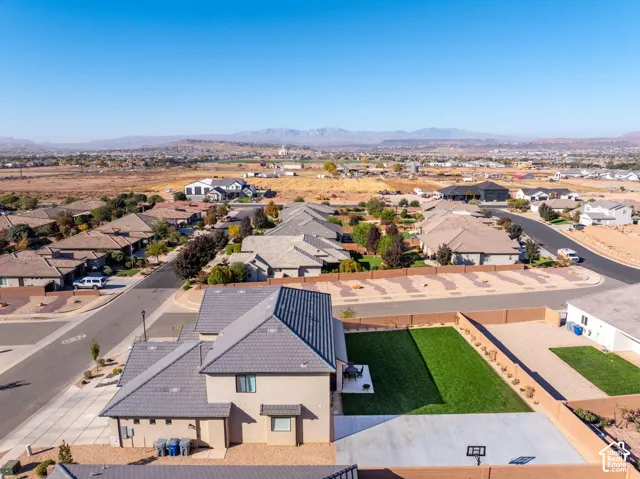 Aerial perspective of a multi-level residence featuring a concrete tile roof, a private backyard with manicured lawn, a concrete patio, and surrounding mountain scenery