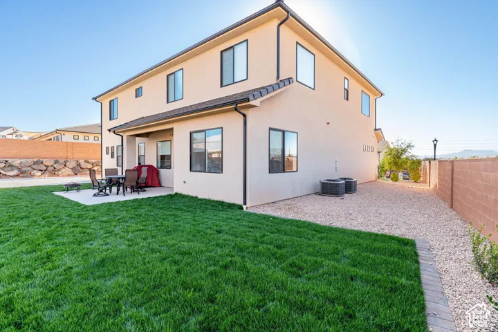 Stucco exterior featuring a covered patio, manicured lawn, stone retaining wall, and gravel side yard