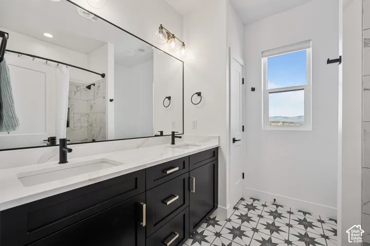 Bathroom featuring a dual-sink vanity with dark cabinetry, white countertops, matte black plumbing fixtures, and patterned tile flooring