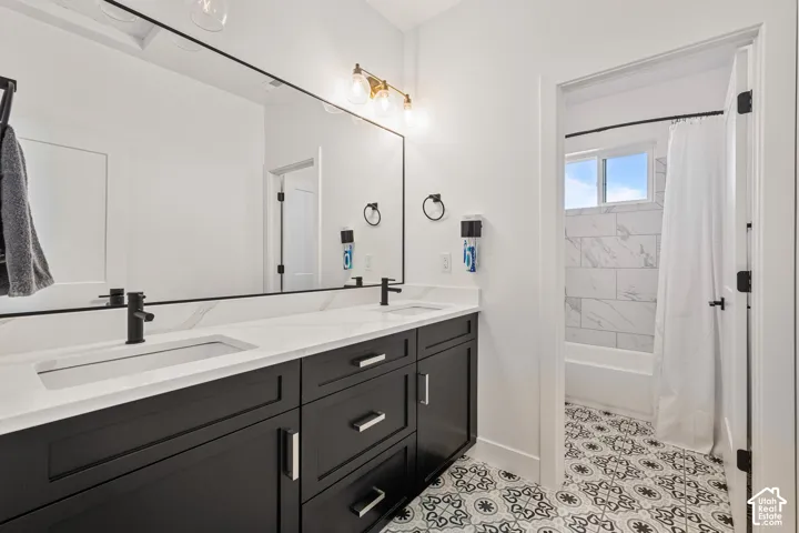 Bathroom featuring a dual-sink vanity with a stone countertop, matte black faucets, patterned tile flooring, and a tub-shower combination with marble-finish wall tile
